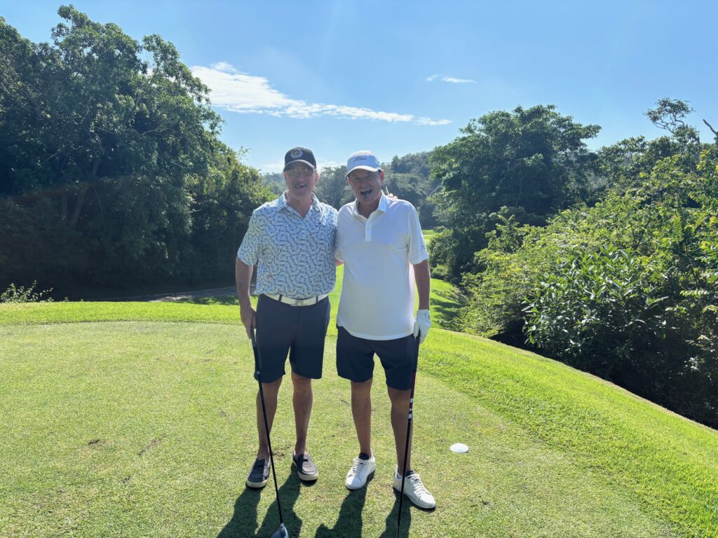 Devin Doyle standing with a friend on a scenic golf course while holding golf clubs.