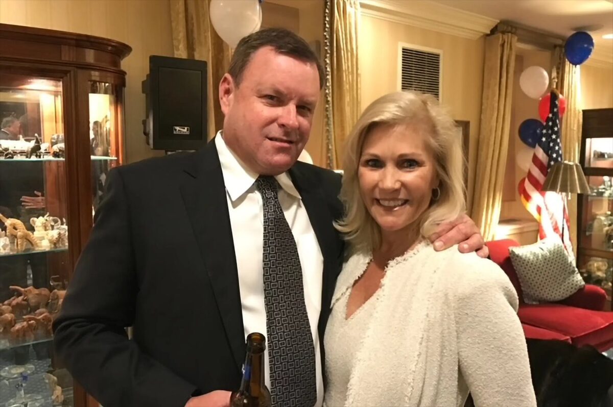 Devin Doyle and his wife posing together at an indoor celebration with an American flag in the background.